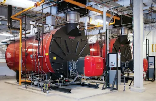 Fully operational industrial boiler system showing the control panel, connected piping lines, and combustion air blower.