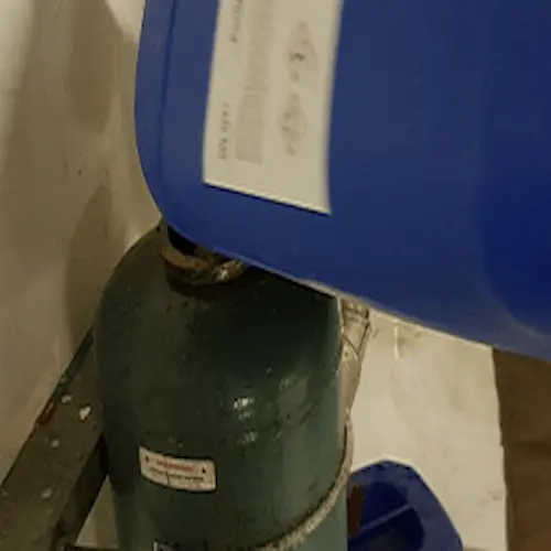 HVAC technician adding water treatment chemicals directly into a bypass pot feeder for a chilled water system.