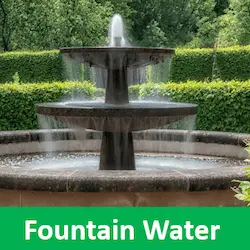 A close-up of a bubbling fountain with a soft green tree background for good fountain water treatment