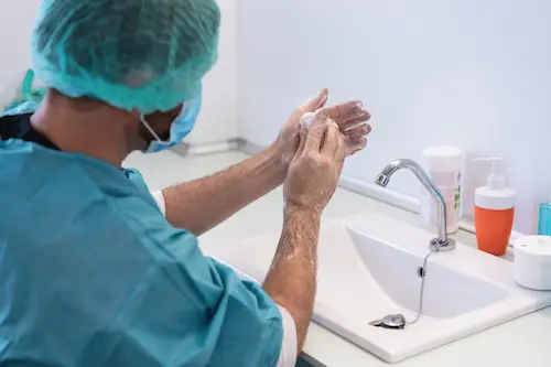A surgeon washes his hands at a scrub sink in a hospital operating room after a surgery