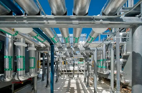Thick insulated industrial pipes mounted on  pillars outside a factory.