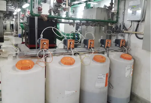 Complete cooling tower chemical dosing system installed in a pump room featuring a digital controller, dosing pumps, and chemical storage tanks.