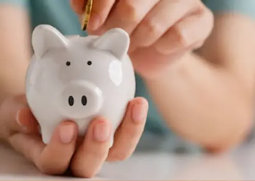 Hand putting a coin into a piggy bank, symbolizing the financial savings achieved through efficient water treatment.